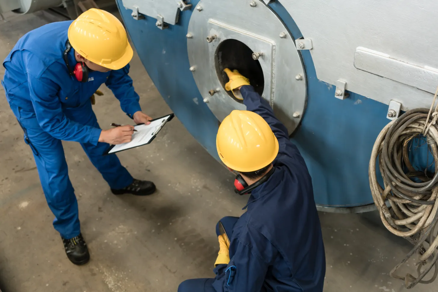 Two technicians conducting commercial boiler inspection requirements check in an industrial facility
