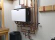 Wall-mounted hydronic boiler system with copper pipes and components installed in a utility room.