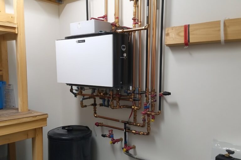 Wall-mounted hydronic boiler system with copper pipes and components installed in a utility room.